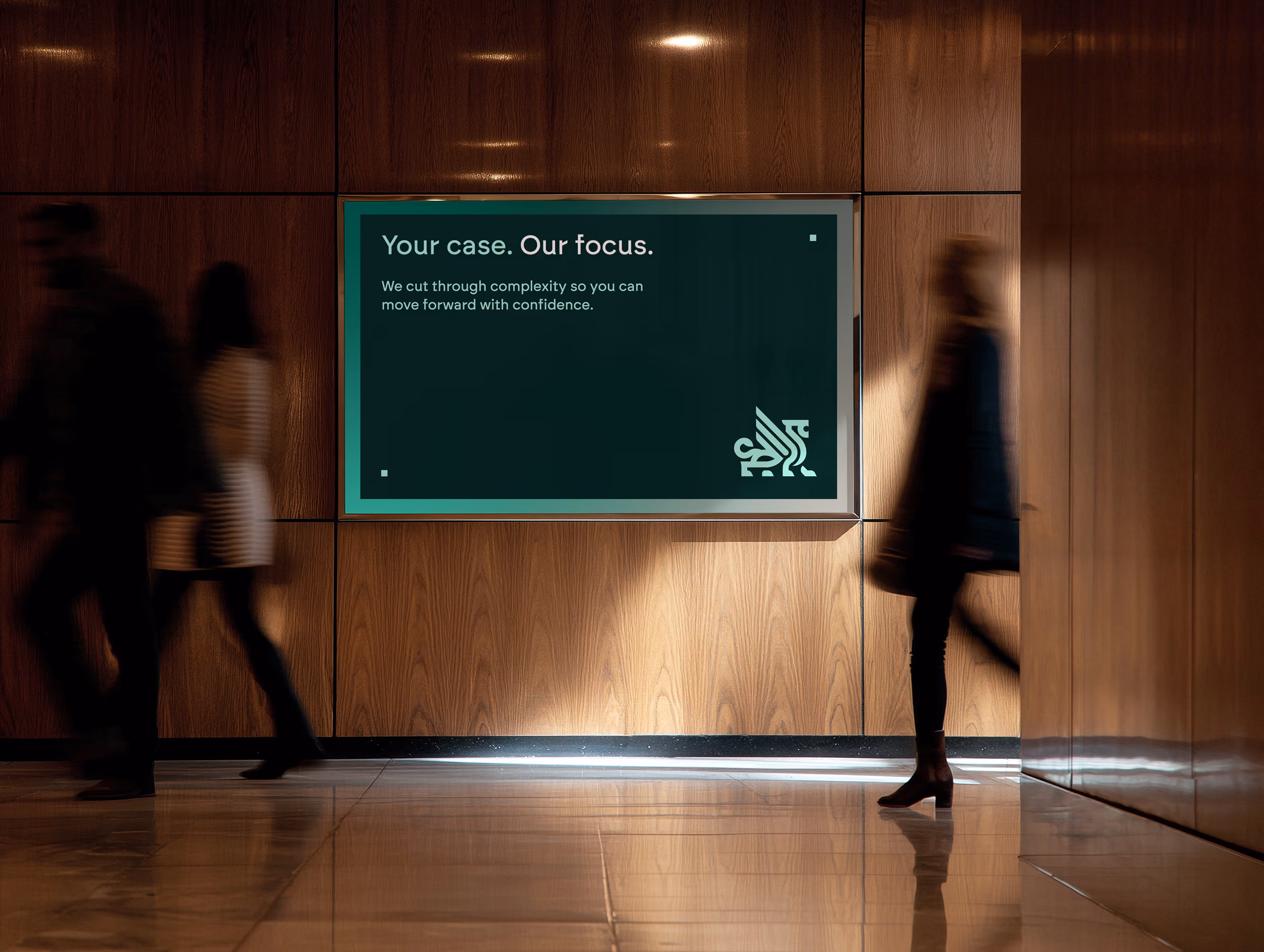 A dark green sign on a wood-paneled wall in a hallway reads: 'Your case. Our focus. We cut through complexity so you can move forward with confidence.' Blurred silhouettes of three people walk past the sign.